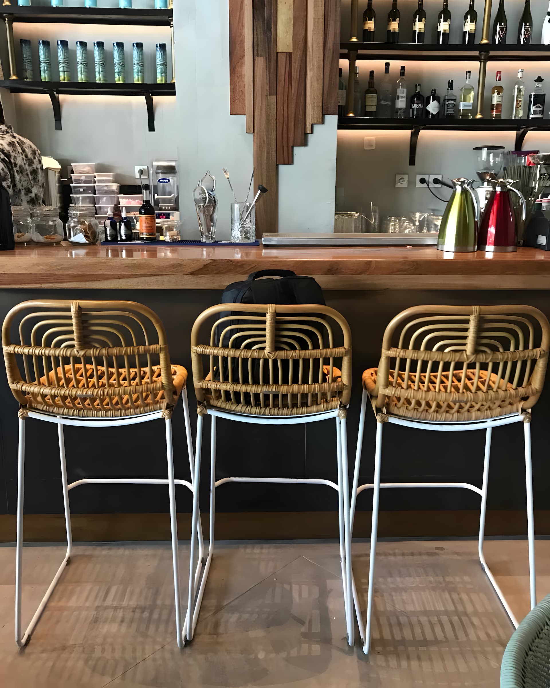 Aitor Rattan Bar Stool with white metal legs in front of bar table - Mellowdays Furniture